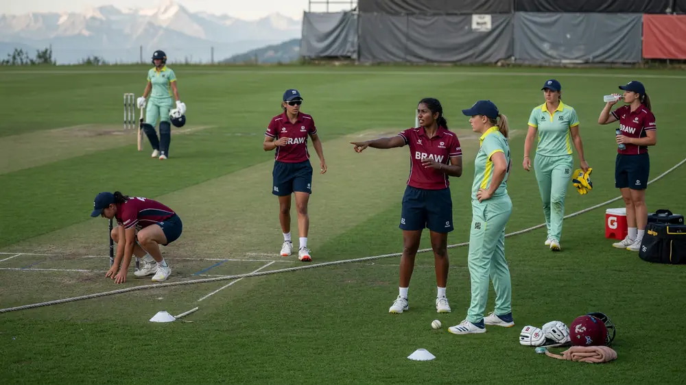 Fielders and a bowler set in a tactical ring on a grass cricket outfield during a women's match